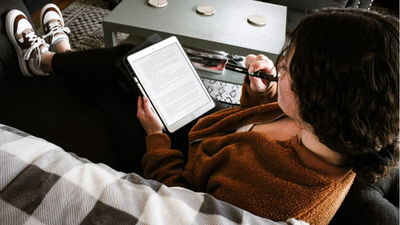 Woman sitting on a couch using a Kindle.