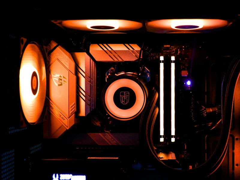 Close-up of a gaming PC showing a CPU cooler, RAM, and fans in orange lighting