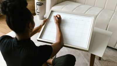 Woman sitting in the floor writing on a wall calendar.