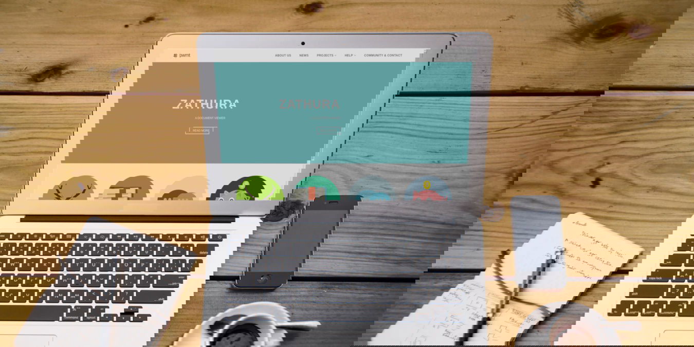 A photograph of a laptop on a table along a cup of coffee, smartphone and notepad.